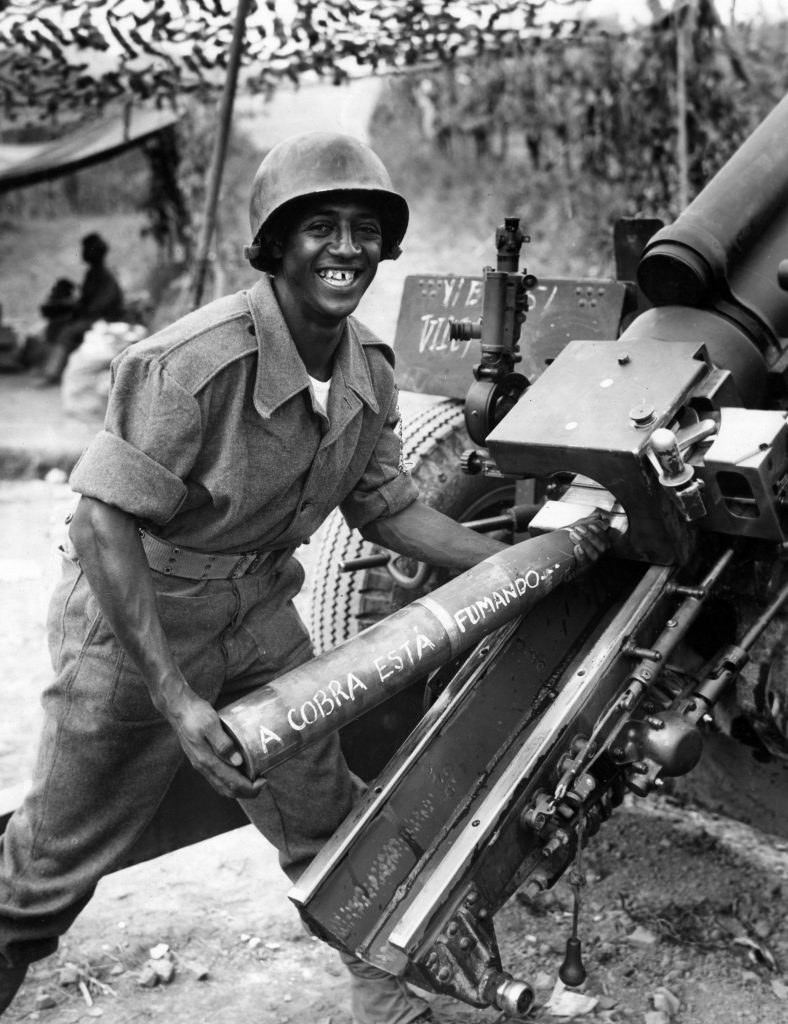Smiling Brazilian soldier holding a shell that reads "A cobrá esta fumando..."